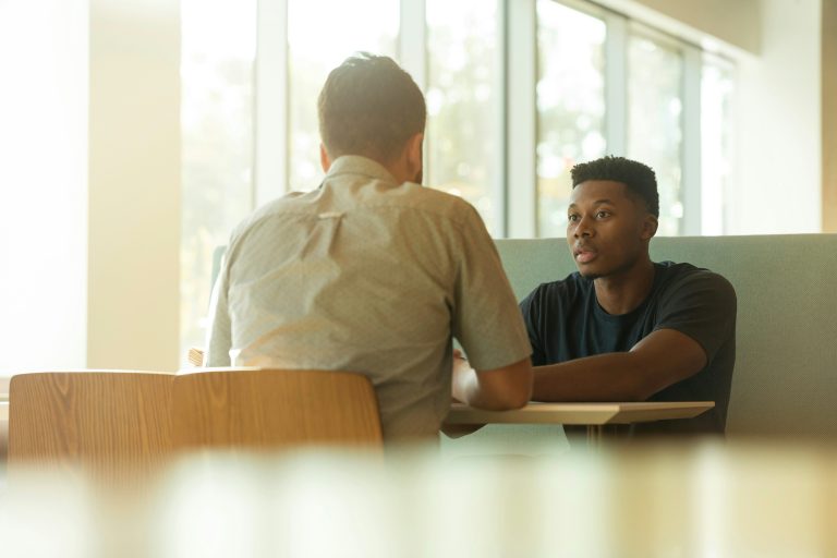 Two people facing each other in conversation across a desk