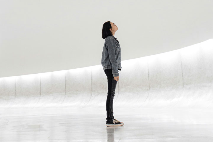 Individual standing thoughtfully in an open, light-filled space, representing career coaching, reflection, and future direction.